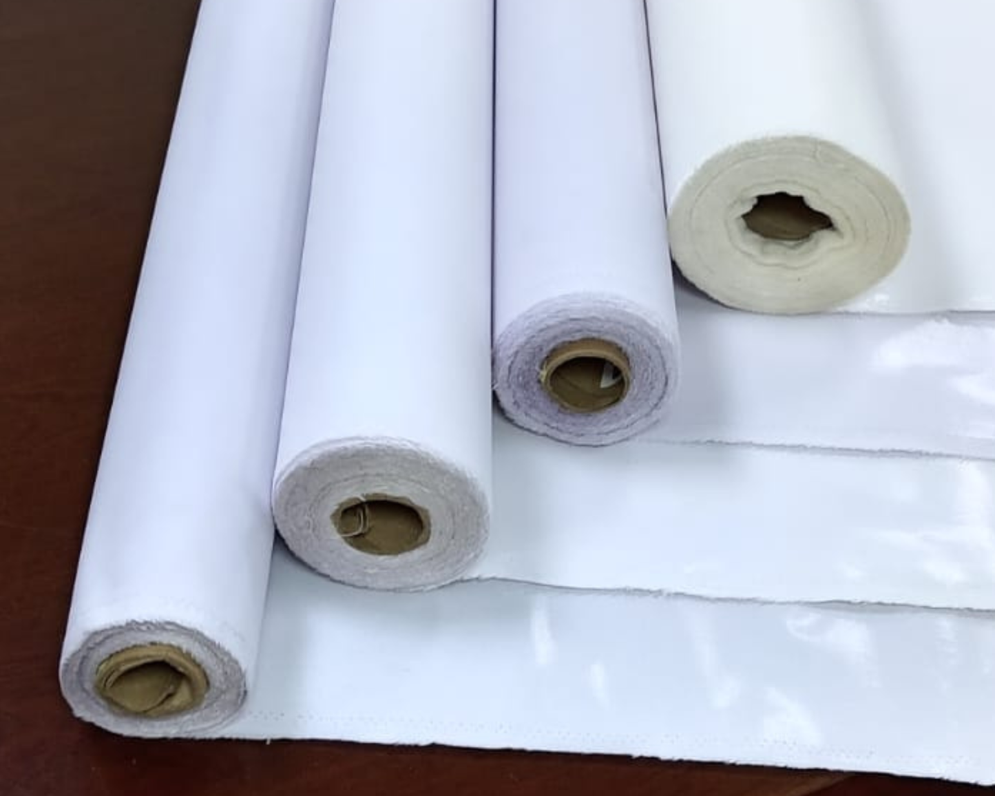 Rolls of shades of white interlining material on a wooden surface