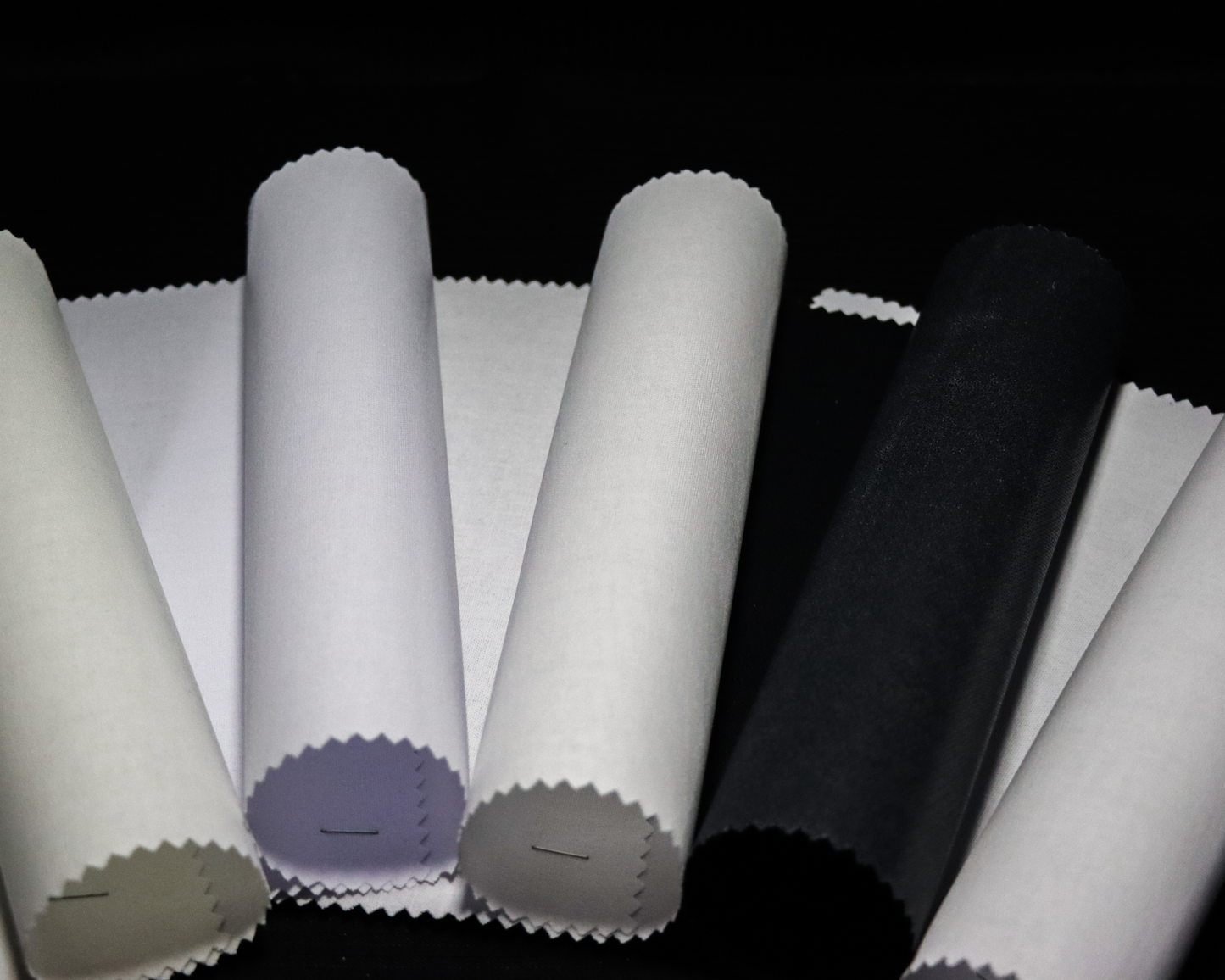 Rolls of IF2777 fabric interlining in various colors on a black background